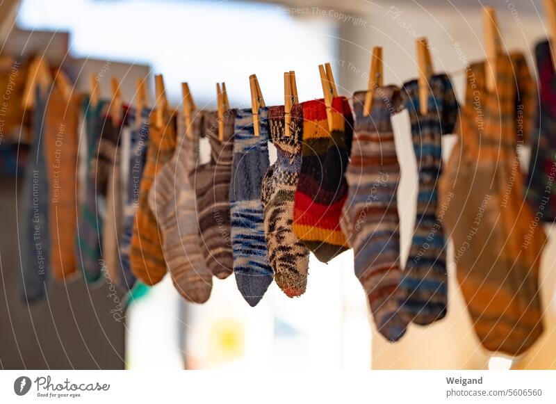 Brightly patterned, home-knitted warm socks in all colors hang neatly side by side on a clothesline, fastened with wooden clothespins knitted socks Winter