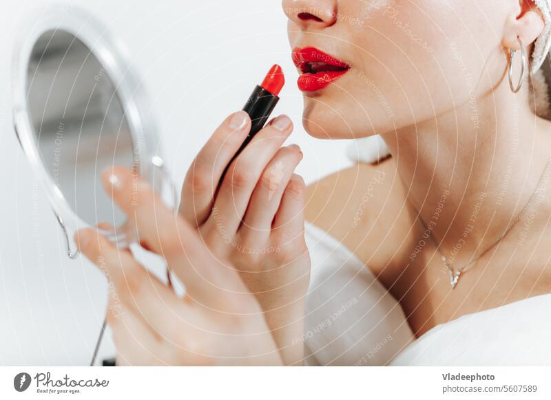 Beautiful young applying red lipstick, holding makeup mirror, towel wrapped on head. Close up view woman self caucasian love routine cosmetics close up make up