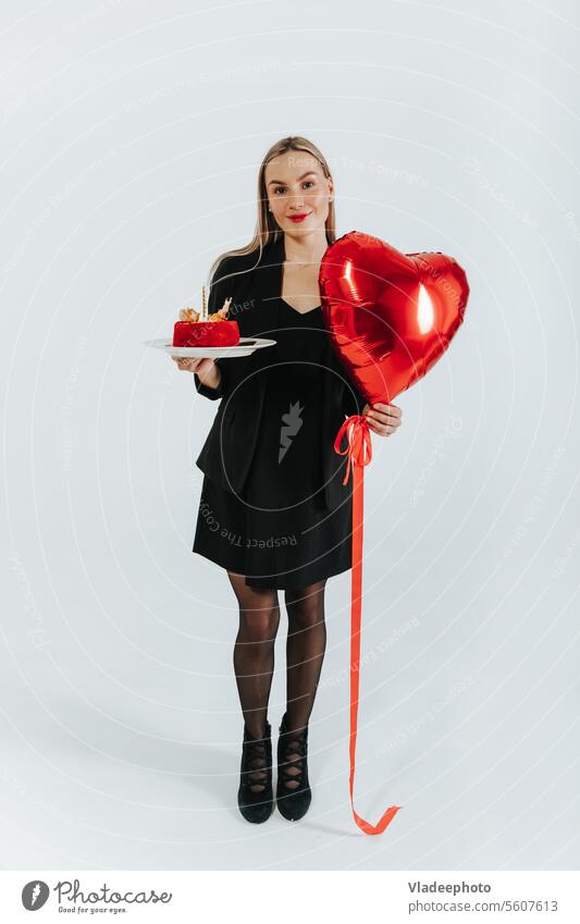 Young woman wearing black jacket and skirt holding heart shape balloon and cake on white background celebrate beautiful red love young symbol suit office