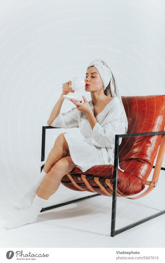 Woman in bathrobe drinking coffee or tea, wrapped in white towel around head. White background woman blanket morning home lifestyle bedding girl lady cozy