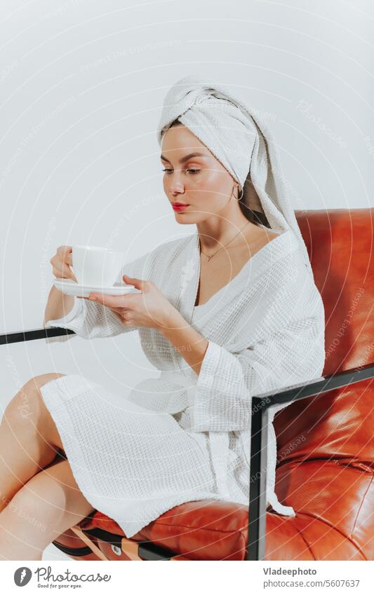 Woman in bathrobe drinking coffee or tea, wrapped in white towel around head. White background woman morning home lifestyle bedding girl lady cozy wellness