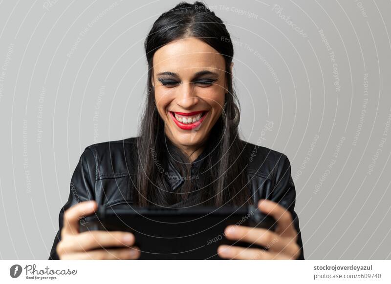 A young woman, with red lipstick, laughs happily as she plays with a handheld video game console she holds in her hands playing videogame fun smile happy female