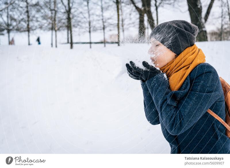 A woman blows snow, collected in the palm of her hand against the background of snow-covered nature winter cold happiness happy joy female people person adult
