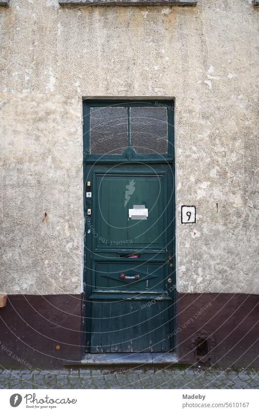 Beautiful old wooden front door in green with house number nine in old faded facade as part of the Unesco World Heritage Site in the alleys of the old town of Bruges in West Flanders in Belgium