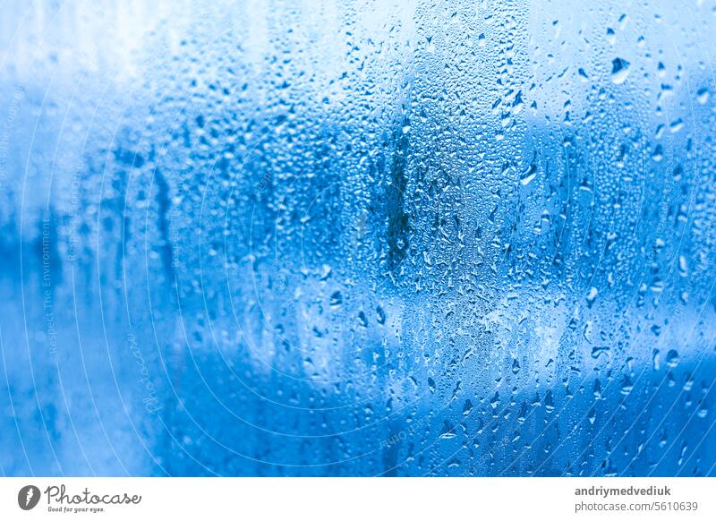 Blue background of glass of metal-plastic window with water droplets condensation indoors room. High humidity. Moisture condensation problems, hot water vapor condensed on window in cold season.