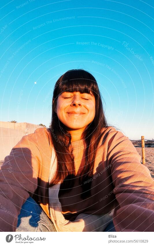 Selfie of a contentedly smiling woman with closed eyes in the morning sun against a blue sky Woman Closed eyes Smiling Sun Contentment portrait To enjoy