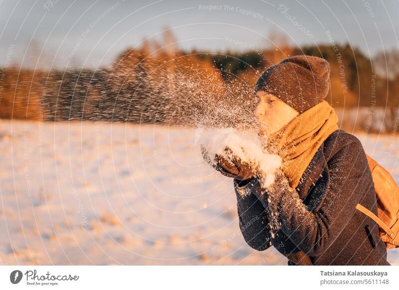 A woman blows a handful of snow from her hands at sunset in the evening winter female people person European White adult mid adult one Single person orange cold