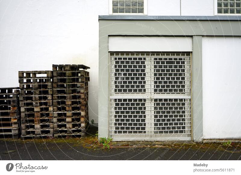 Stacked wooden euro pallets in front of a white building with a barred door on the yard of a winegrower in Traben-Trarbach on the Moselle river in the district of Bernkastel-Wittlich in Rhineland-Palatinate, Germany