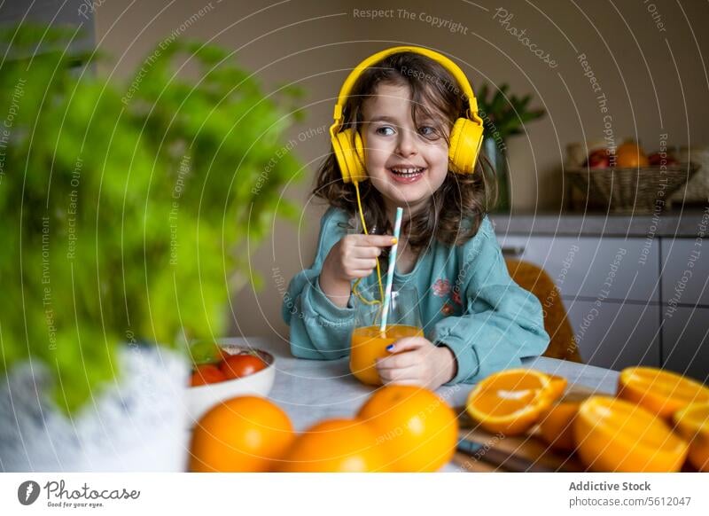Caucasian child having juice at home girl smiling glass looking away listening music technology headphones straw selective focus lifestyle leisure food domestic