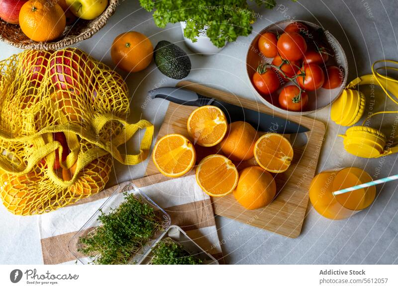 Organic fruits and tomatoes on table orange healthy tangerine high angle juice glass mesh bag home knife chopping board slice napkin technology headphones box