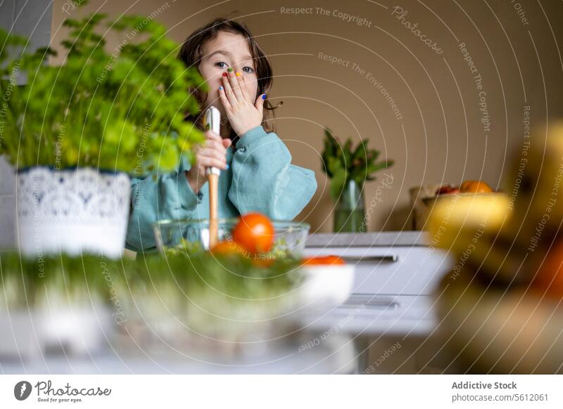 Elementary kid preparing salad at home girl cute fingernail colorful covering mouth hand kitchen portrait caucasian surprise selective focus person lifestyle