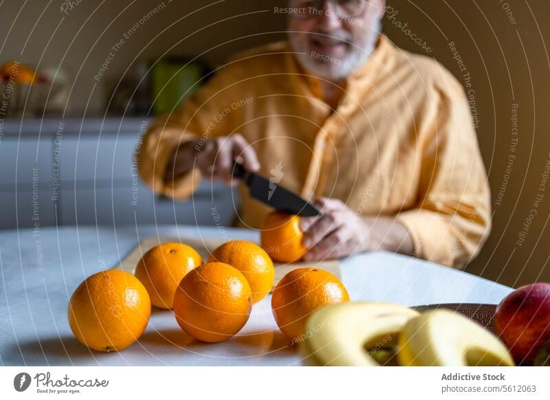 Elderly male cutting oranges at home man senior knife fruit table fresh organic kitchen preparing caucasian selective focus person lifestyle leisure activity