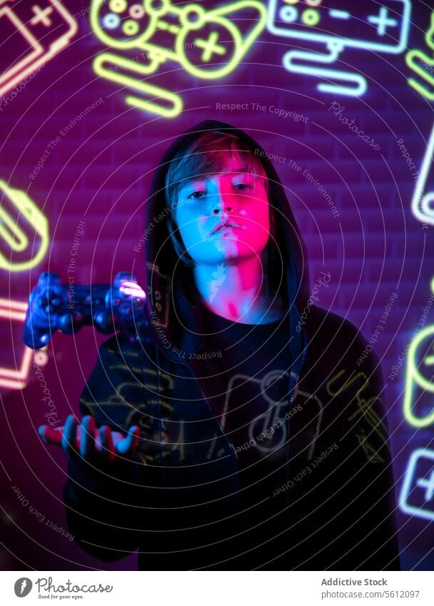 Teenage gamer with controller in neon-lit room teenager neon light gaming symbol youth electronic entertainment video game leisure activity hobby indoor glow