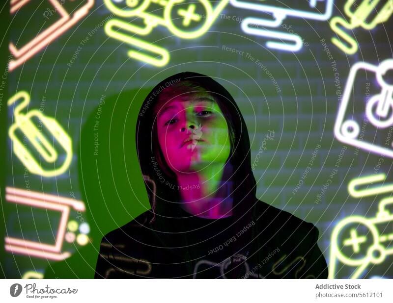 Youth boy illuminated by colorful neon graphics youth light background person contemplative expression vibrant face urban mood nighttime style hoodie fashion