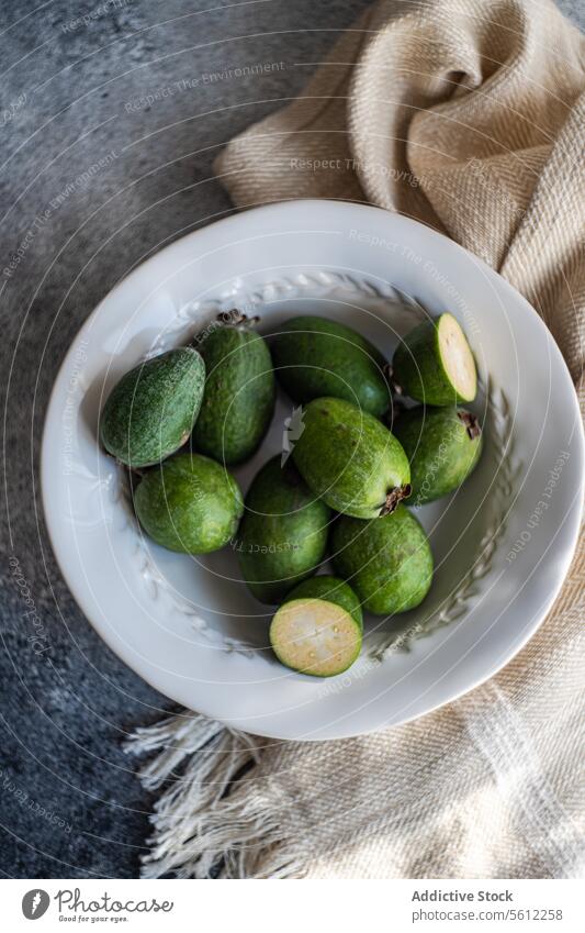 Fresh Feijoa Fruits on a Ceramic Plate feijoa fruit fresh raw ceramic plate green half-cut pulp rustic textured background food nutrition exotic tropical