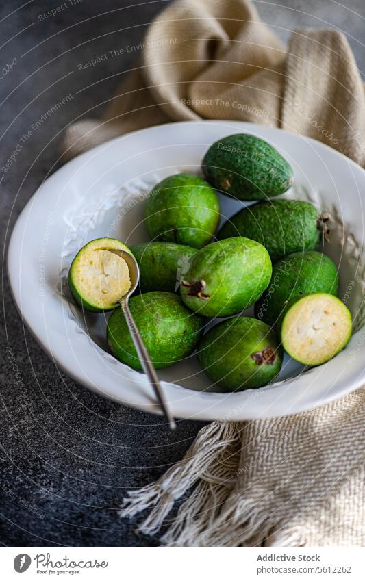 Fresh feijoa fruits in a white bowl on a rustic background ceramic ripe fresh cut open textured napkin dark composition food green exotic tropical healthy diet
