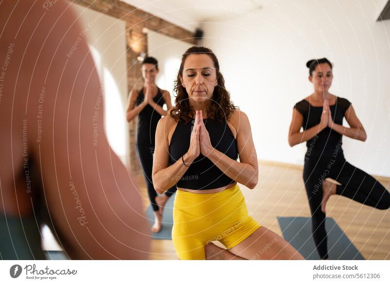 Group yoga practice session in a bright studio woman group balance exercise fitness health well-being concentration posture class mat instructor relaxation