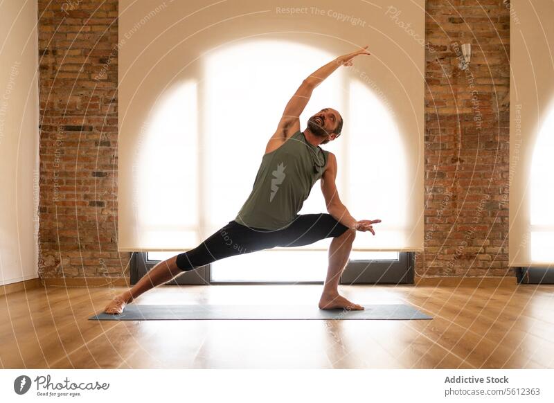 Man practicing yoga in a sunny studio man pose mat exercise peaceful well-lit brick wall wooden floor health wellbeing fitness practice serene balance