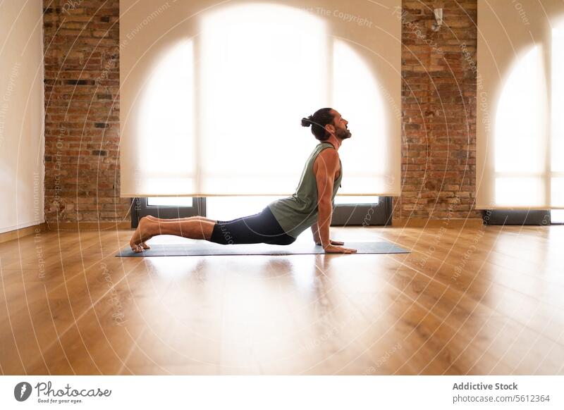 Man practicing yoga in a sunlit room man stretch mat hardwood floor exposed brick natural light peaceful wellness fitness health exercise meditative tranquility