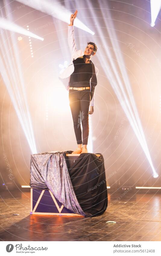 Magician performing trick while standing on box man magician show fabric illusion arm raised male performer illusionist conjurer stage mystery concert theater