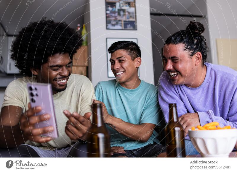 Male friends see a photo in smartphone at home smile afro hair leisure together living room friendship weekend mobile beer bottle cheerful happy looking
