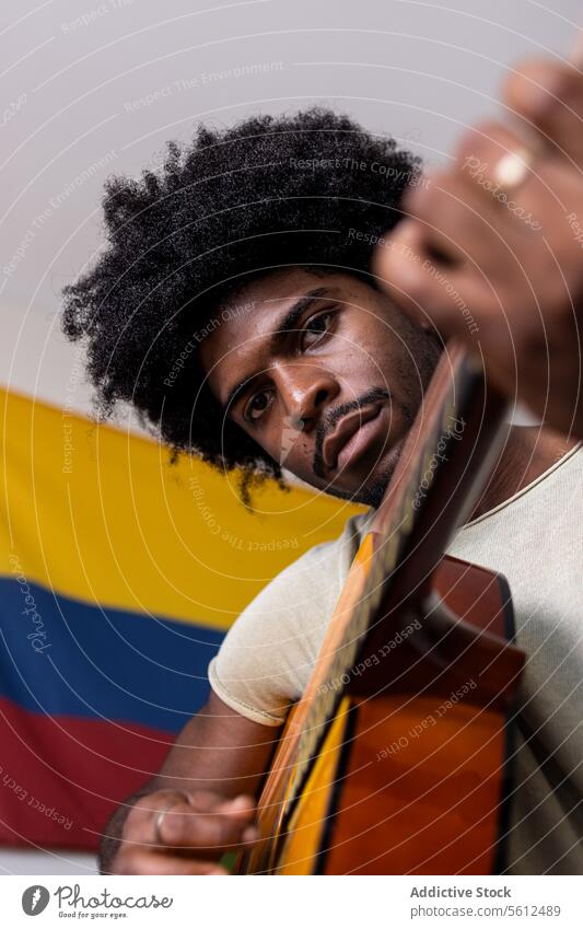 Serious man playing guitar at home young practice portrait colombian flag from below confident serious looking at camera afro hair sit focus acoustic string