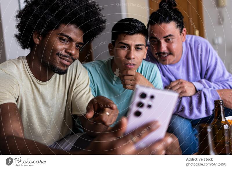Male friends taking selfie at home smile afro hair smartphone leisure together living room friendship weekend mobile beer bottle looking cellphone social media