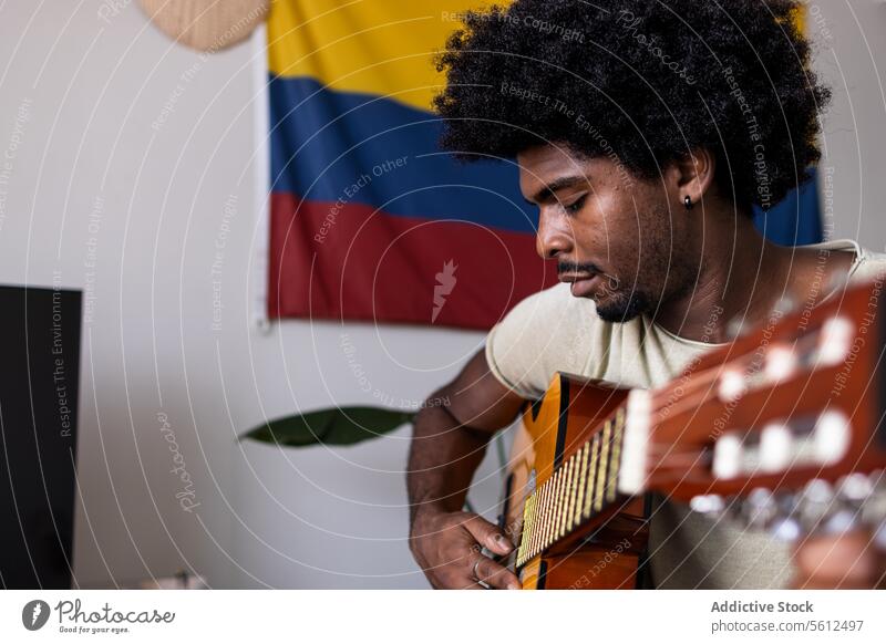 Serious man playing guitar at home young practice portrait colombian flag confident serious afro hair sit focus acoustic string instrument weekend closeup