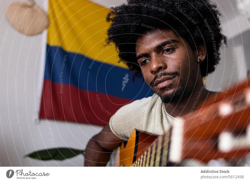 Serious man playing guitar at home young practice portrait colombian flag confident serious looking away afro hair sit focus acoustic string instrument weekend