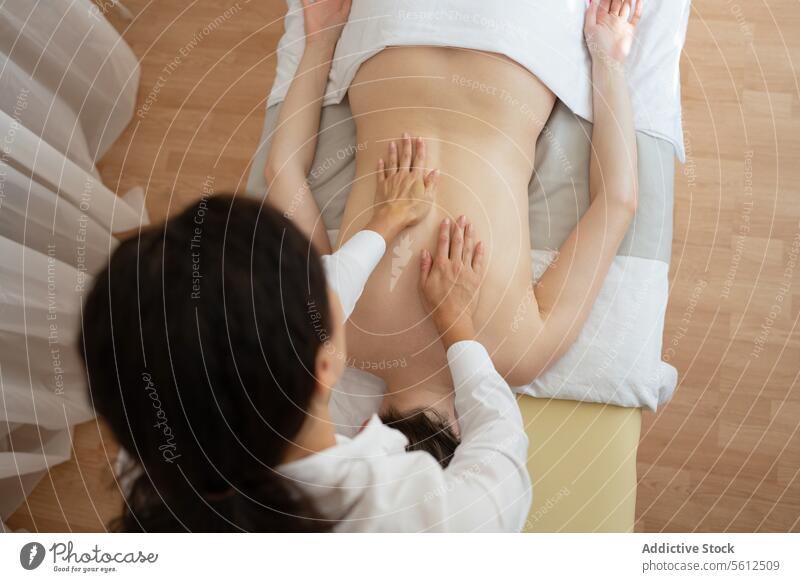 Top view of crop unrecognizable masseuse doing back massage to anonymous female client lying on table during session in modern spa salon hand top view therapist