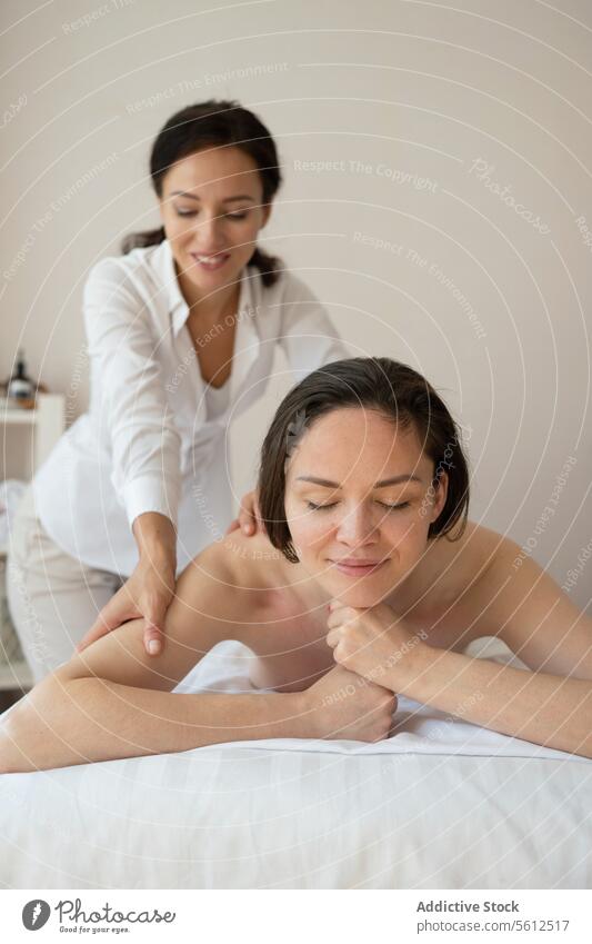 Beautiful topless female customer smiling lying comfortably on bed and receiving back therapy massage from woman therapist in spa salon women beautiful enjoy