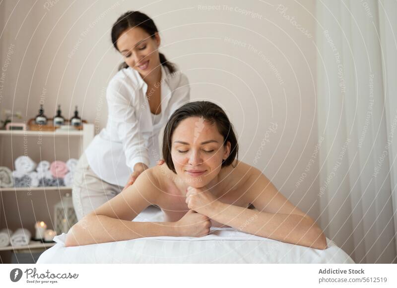 Beautiful topless female customer smiling lying comfortably on bed and receiving back therapy massage from woman therapist in spa salon women beautiful enjoy