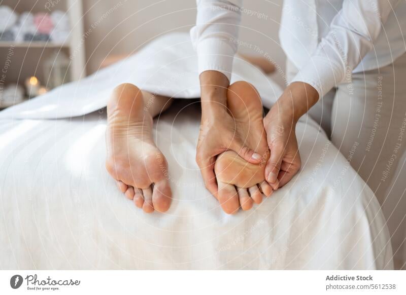 Crop hands of anonymous female therapist massaging foot of customer lying on bed to relieve pain by gently pressing pressure points at spa salon massage gentle
