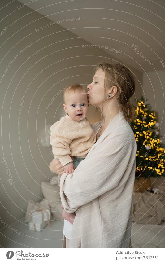 Tender moment between mother and child at Christmas baby kiss forehead christmas tree twinkling light tender love care affection family holiday celebration