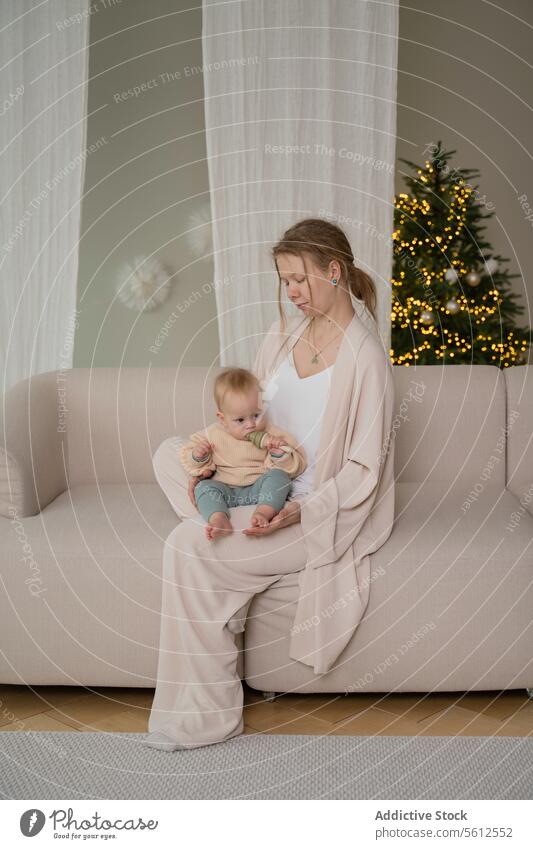 Mother and Baby Enjoying Cozy Time at Home mother baby home couch christmas tree cozy tender moment woman child sitting indoors warm light festive season