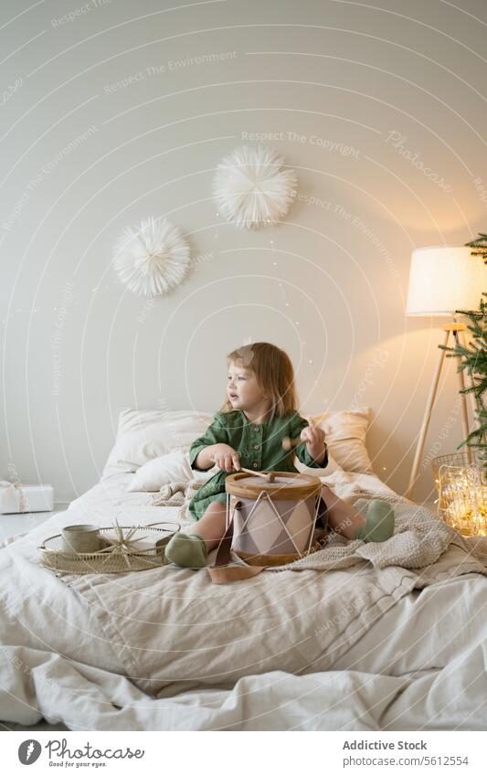 Toddler enjoys drum playtime in a decorative room toddler child bedroom cozy warm light festive decoration green dress indoor fabric lamp cushion comfort