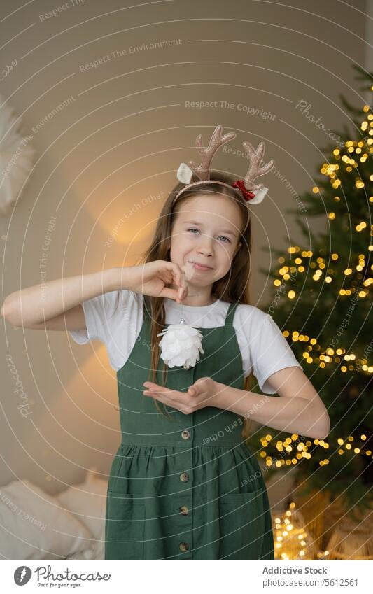 Young girl celebrating Christmas with festive headband christmas reindeer love gesture tree lights glowing celebration joy young child holiday season decoration
