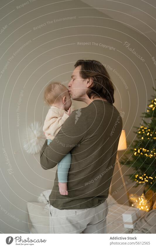 Tender moment between father and child at Christmas man baby kiss christmas tree tenderness festive atmosphere fatherhood bonding love care affection holiday
