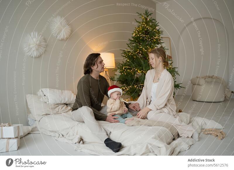 Family enjoying a cozy Christmas morning together family christmas home baby santa hat presents tree special moment young parents holiday celebration decorated