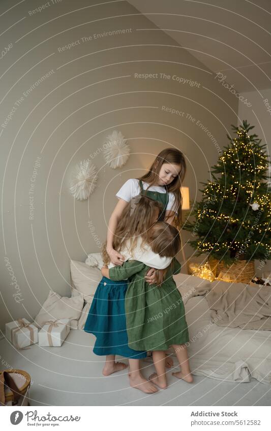 Tender moment of siblings embracing by Christmas tree girl embrace christmas tree cozy holiday warmth family affection tender young room lighting decor festive