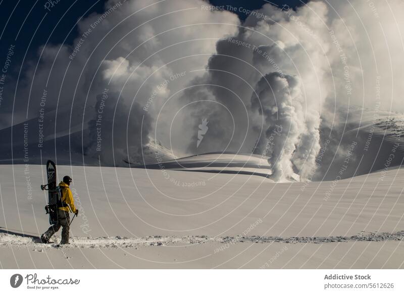 Unrecognizable person with a snowboard walking towards an active volcano eruption in a snowy Japanese landscape winter adventure faceless outdoors nature