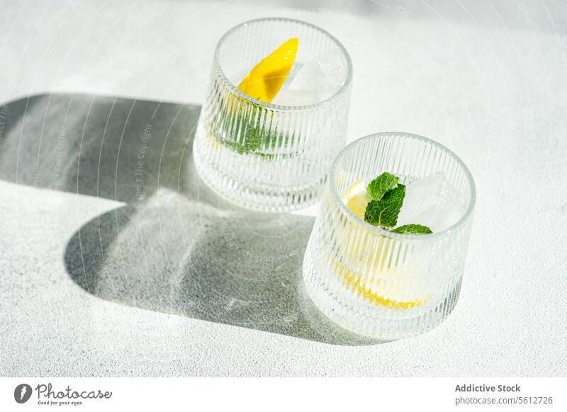 Refreshing gin tonic drinks with lemon garnish beverage mint ice glass cocktail refreshment alcohol mixology citrus herb summer sunlight shadow surface bright