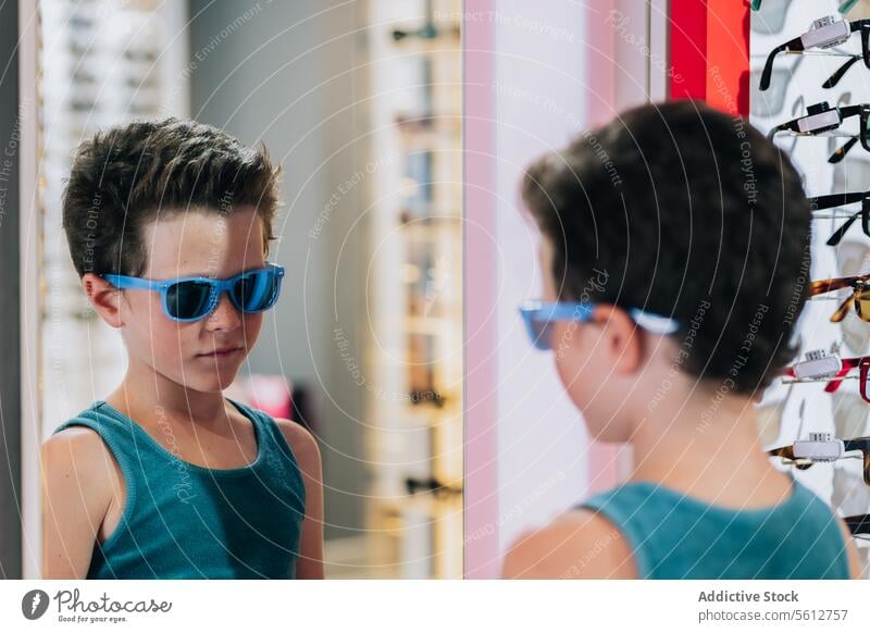 Child trying on blue glasses in store boy sunglasses mirror cute stylish tying on buy eyewear optical reflection lifestyle face tank top attractive calm goggles