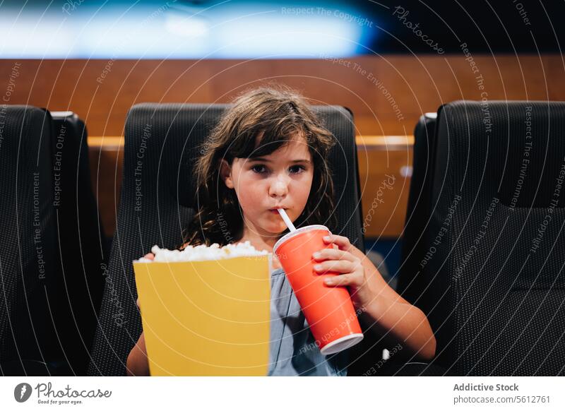 Girl with popcorn enjoying movie in theater girl bucket cute tasty large drinking coke sit black seat watching weekend lifestyle entertain child comfort snack