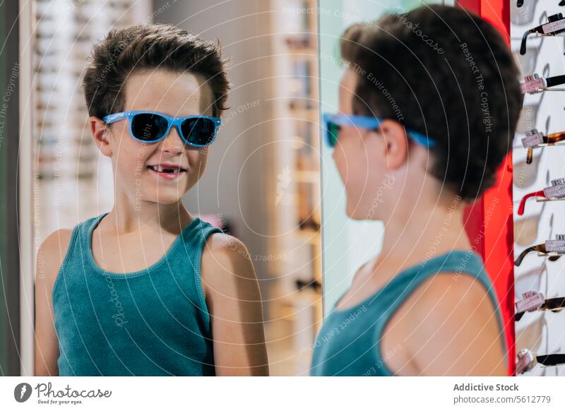 Child trying on blue glasses in store boy sunglasses smile mirror cute stylish eyewear optical reflection lifestyle face tank top attractive calm goggles serene