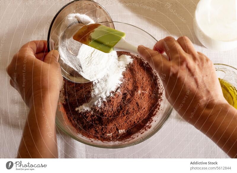 Top view of baking preparation with hands of an unrecognizable person pouring flour into a bowl with cocoa powder recipe sifted white background cooking kitchen