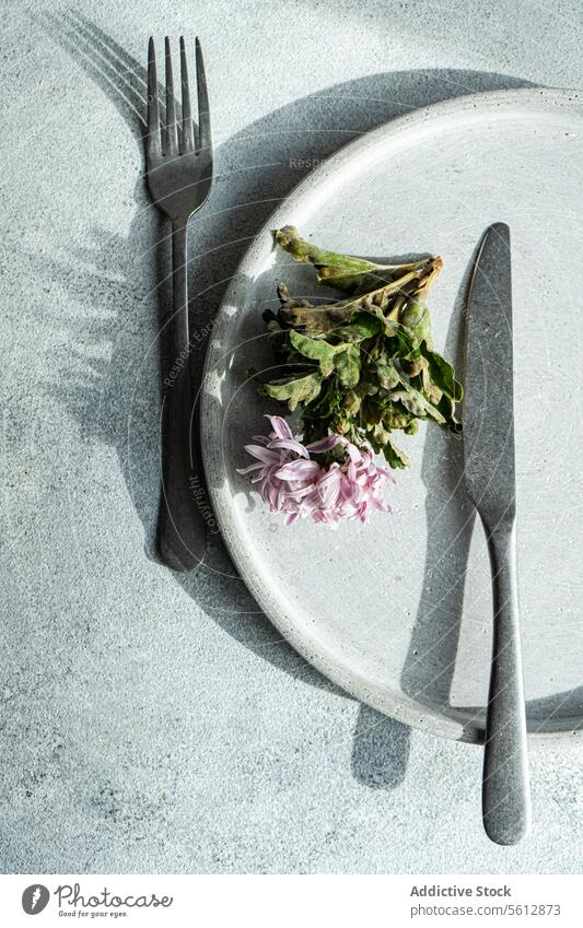 Plate with pink flower and cutlery on a gray background plate fork knife food scraps white textured surface top-down view salad green leaves petals minimal