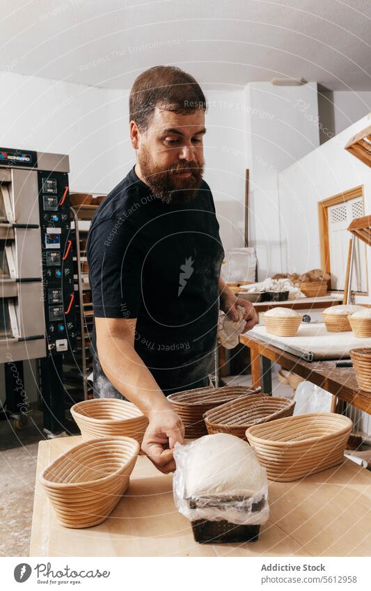 Man covering bread dough in container with plastic baker sourdough mold table bakehouse beard focus professional uncooked raw wooden concentrate kitchen bakery