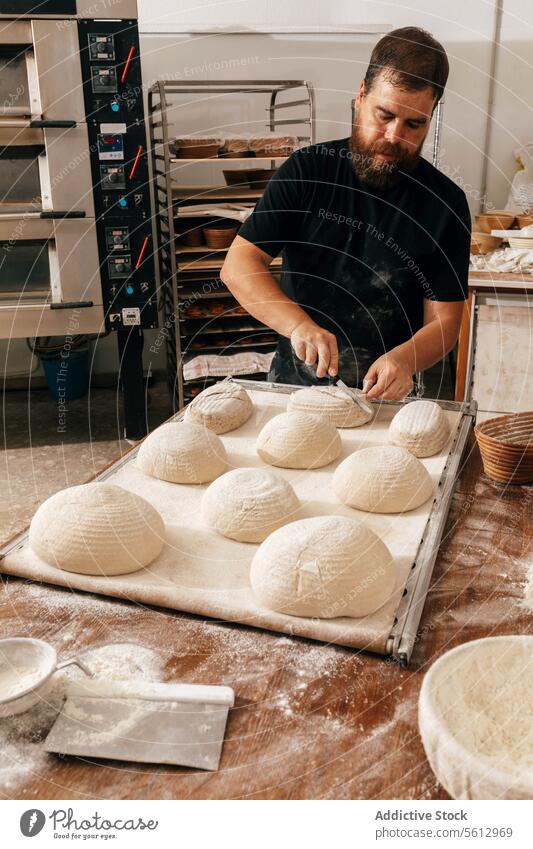 Focused man cutting bread dough in kitchen chef baking tray bakery concentrate serious knife flour table cook focus score beard casual attire fresh prepare