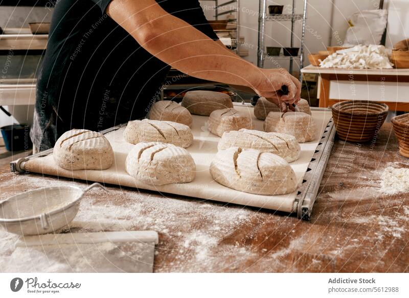 Baker cutting bread dough at table in kitchen chef knife hand crop unrecognizable uncooked baking tray large bakehouse body part score casual attire flour